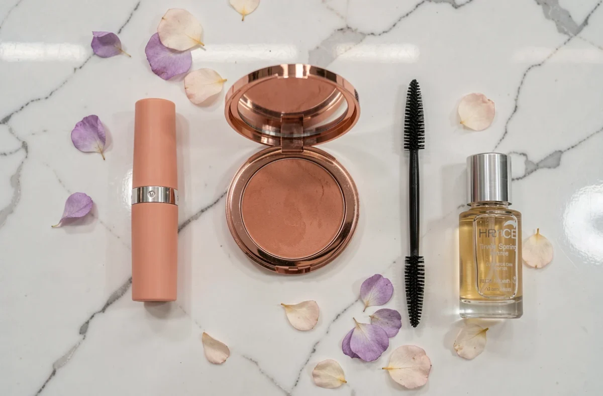 Plat de produits maquillage printemps sur marbre blanc avec pétales de fleurs séchées et teintes corail et rose